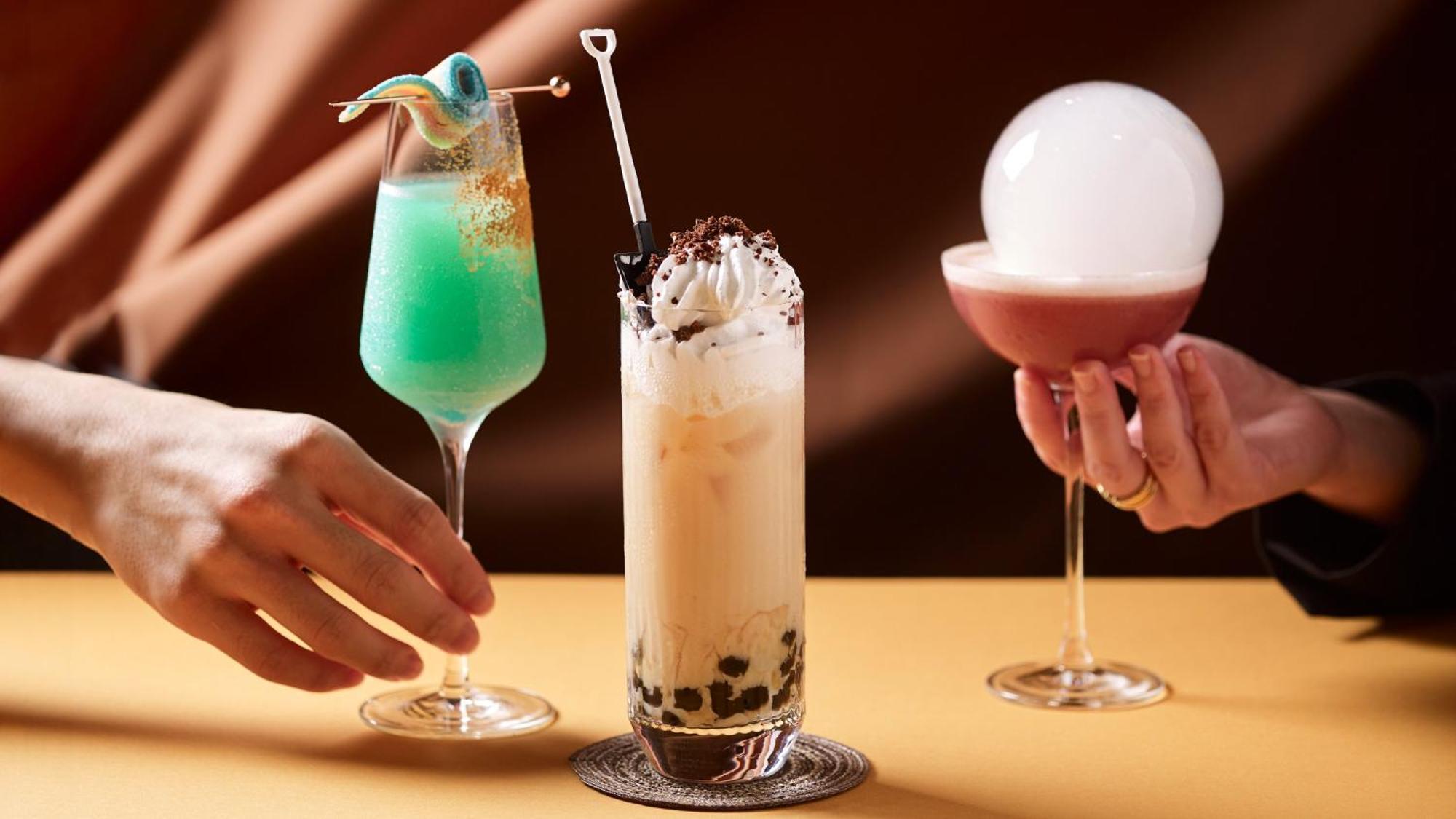 فندق كراون بلازا مطار شانجي سنغافورة المظهر الخارجي الصورة The photo features three colorful and creatively presented cocktails. 

1. On the left, there is a bright green drink served in a tall glass, garnished with a playful decoration, likely a piece of candy or fruit.
  
2. In the center, a tall glass con
