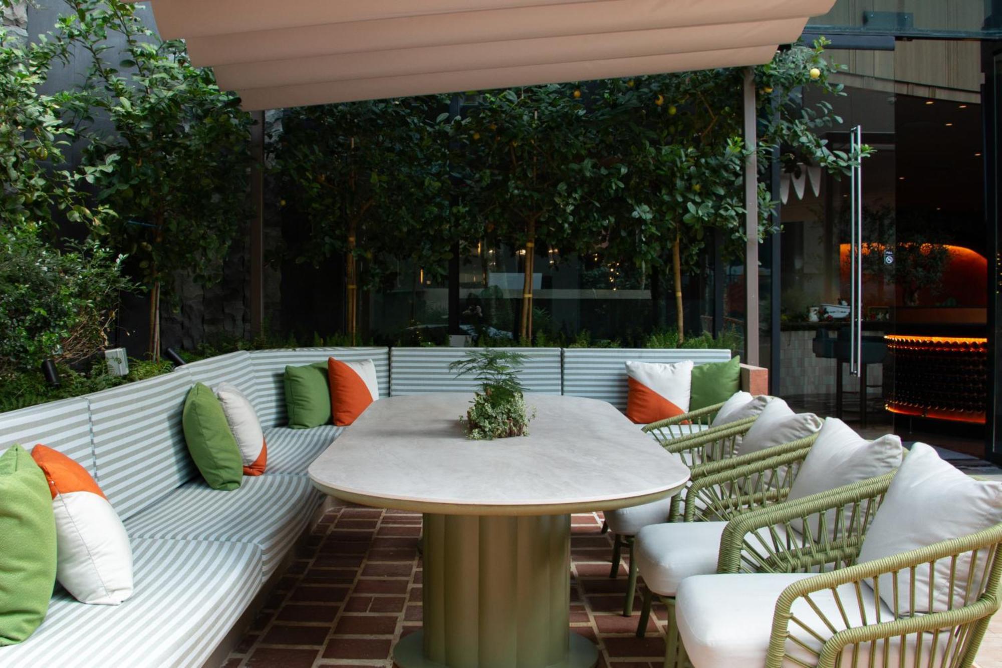 فندق كراون بلازا مطار شانجي سنغافورة المظهر الخارجي الصورة The photo shows a stylish outdoor seating area. There is a large, oval table at the center, surrounded by comfortable chairs with white cushions. The seating features a long, curved bench with a light green and white striped design, and it is adorned