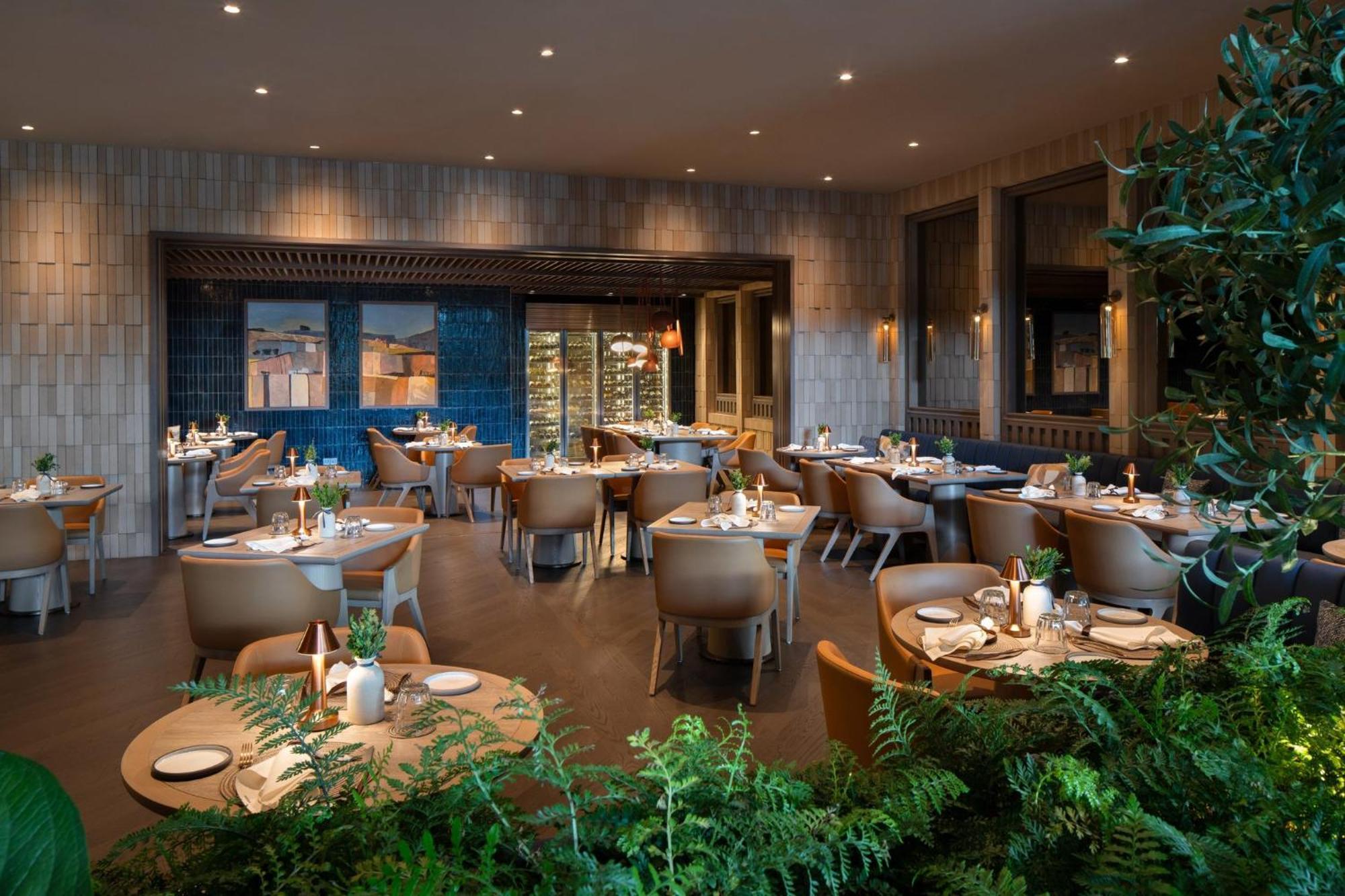 فندق كراون بلازا مطار شانجي سنغافورة المظهر الخارجي الصورة The photo shows an upscale restaurant interior. It features multiple tables set with plates and decorative items, arranged in a spacious area. The design includes modern furnishings, with light wood and neutral tones dominating the decor. There are l