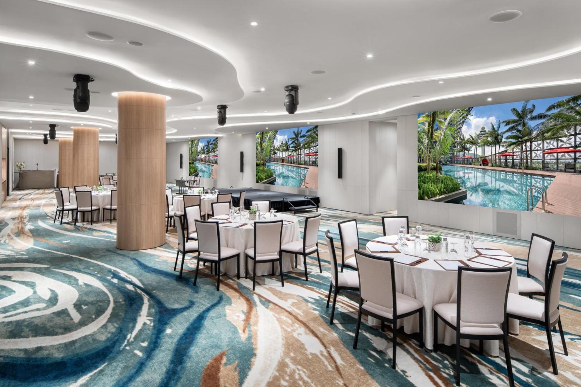 فندق كراون بلازا مطار شانجي سنغافورة المظهر الخارجي الصورة The photo showcases a modern event space or dining area. It features several round tables covered with white tablecloths and set with dishes and utensils. The floor has an eye-catching design with swirling patterns in various shades of blue and beige